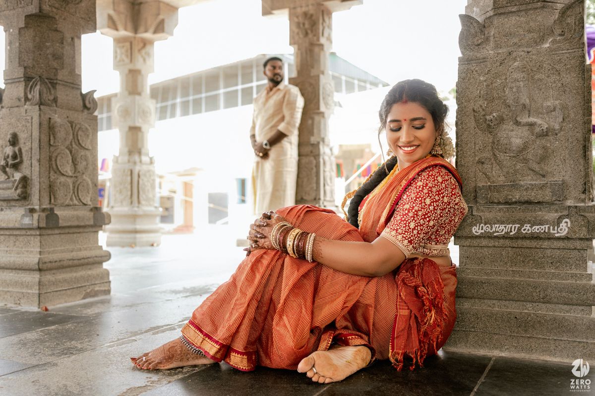 A candid moment captured at a traditional Indian temple with ornate stone pillars and a person wearing an orange sari.