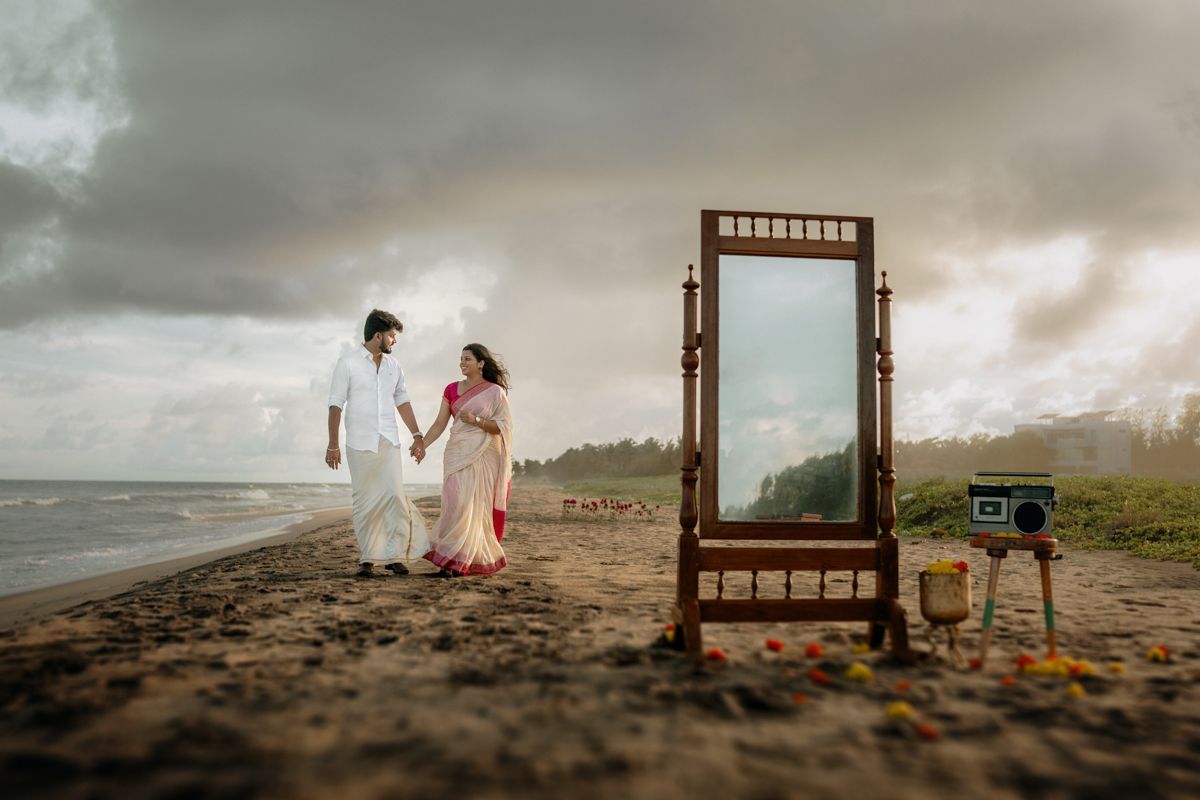 A decorative wooden mirror is positioned on a dark sandy beach with stormy skies in the background.