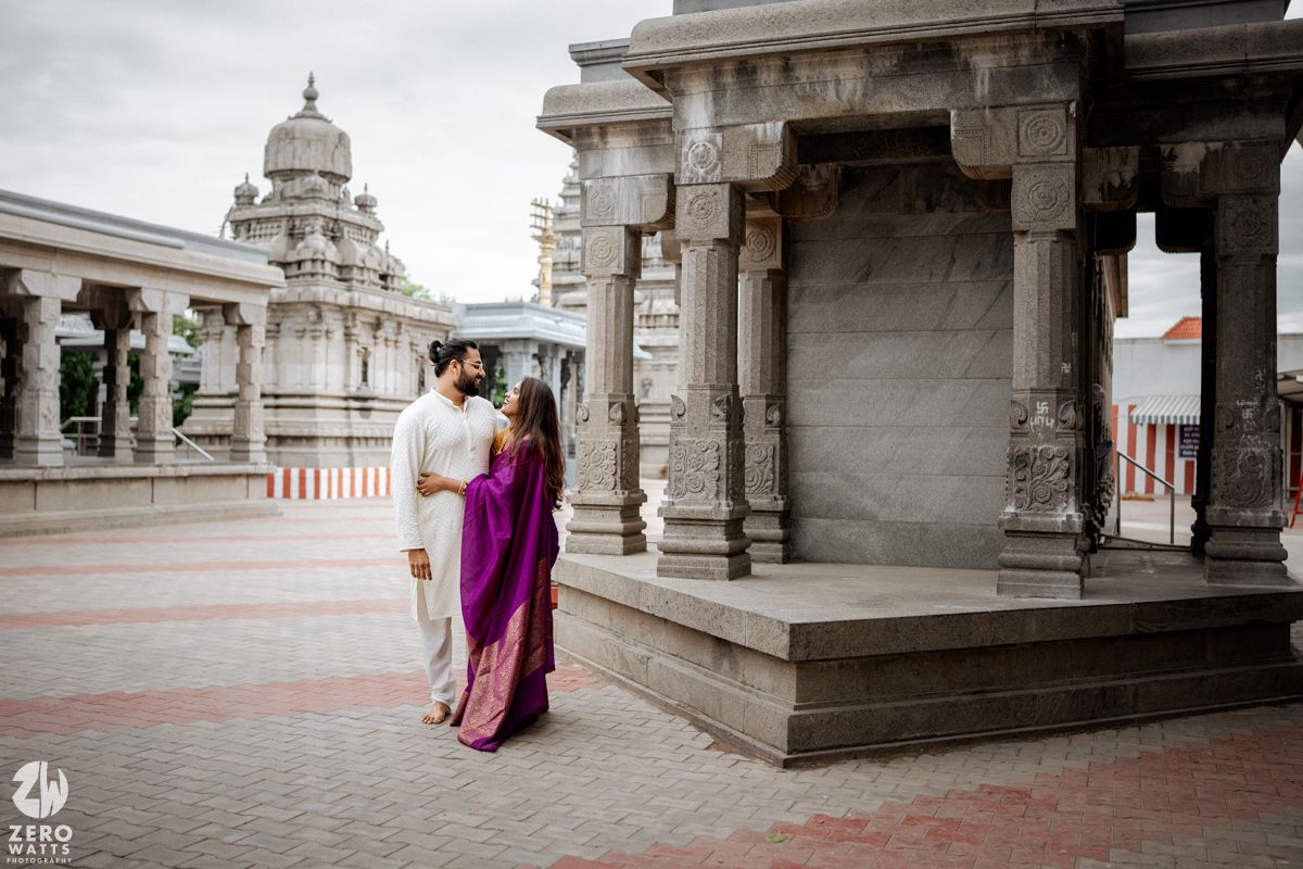 Wide view of a temple complex with stone pillars and a couple in traditional Indian dress.