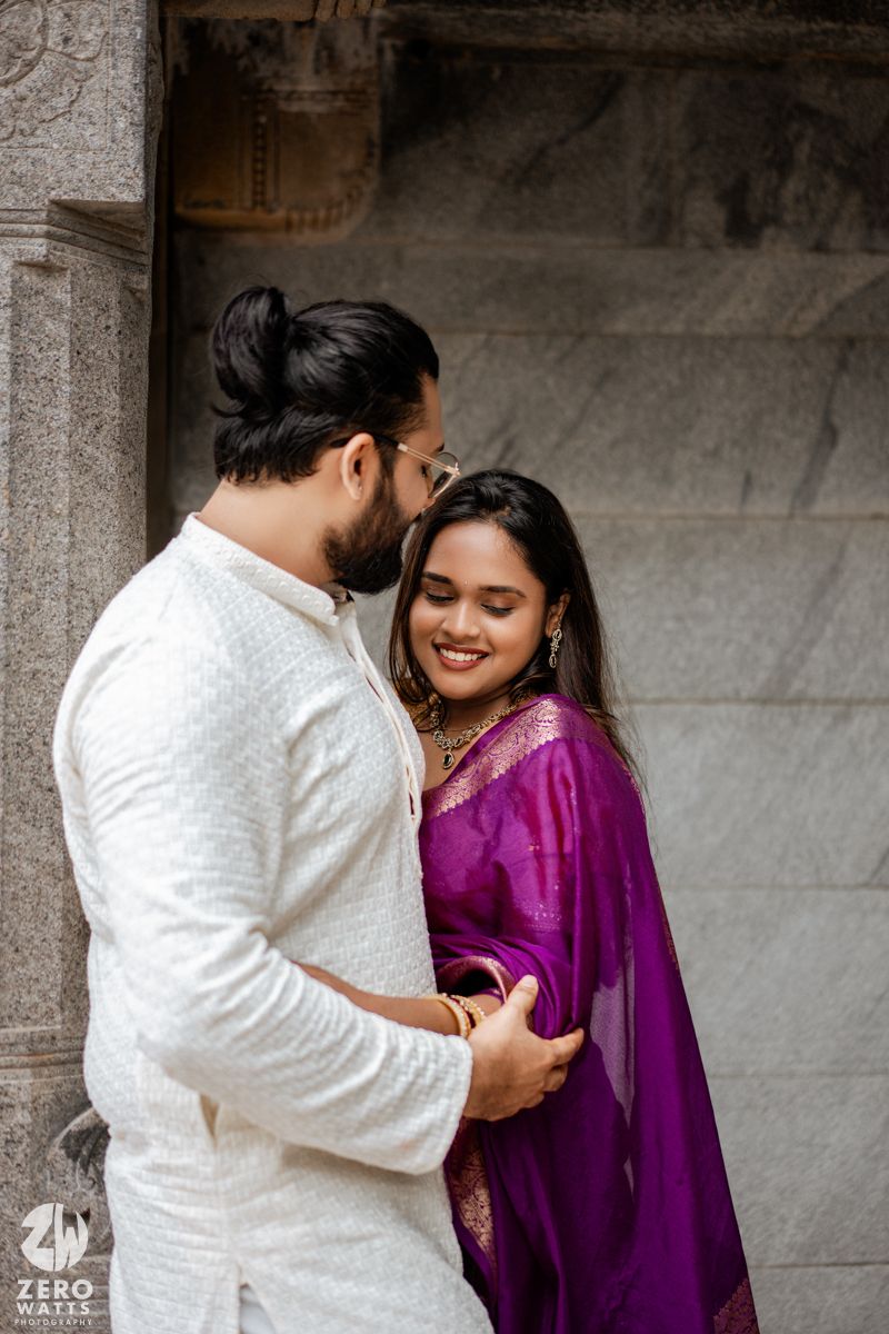 Romantic couple in traditional Indian attire share an intimate moment against stone pillars.