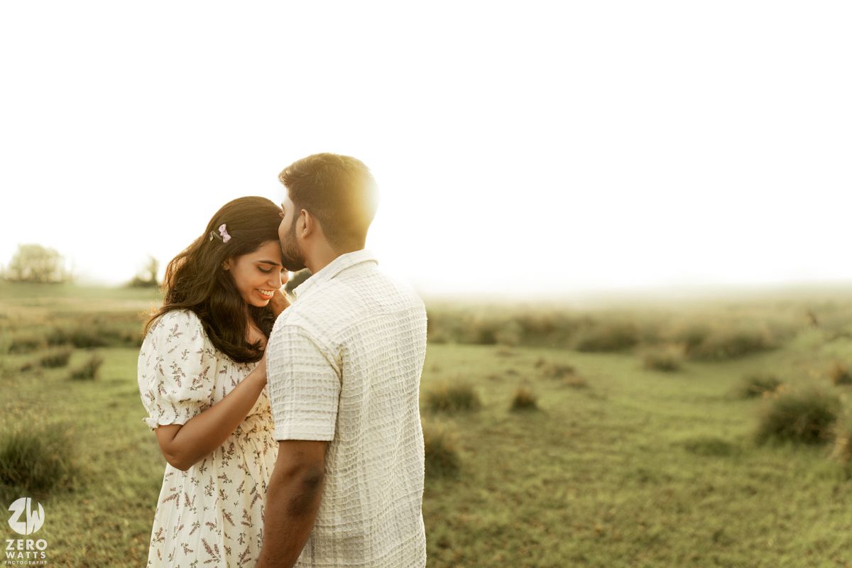 Couple in casual attire sharing intimate moments in a sunny meadow during a romantic outdoor photoshoot.
