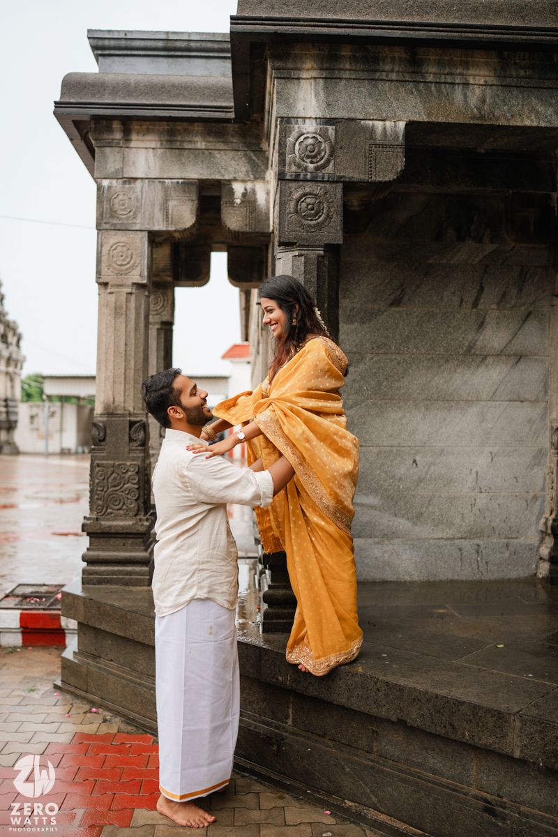 Couple in traditional attire sharing a romantic moment under stone pillars of a temple.