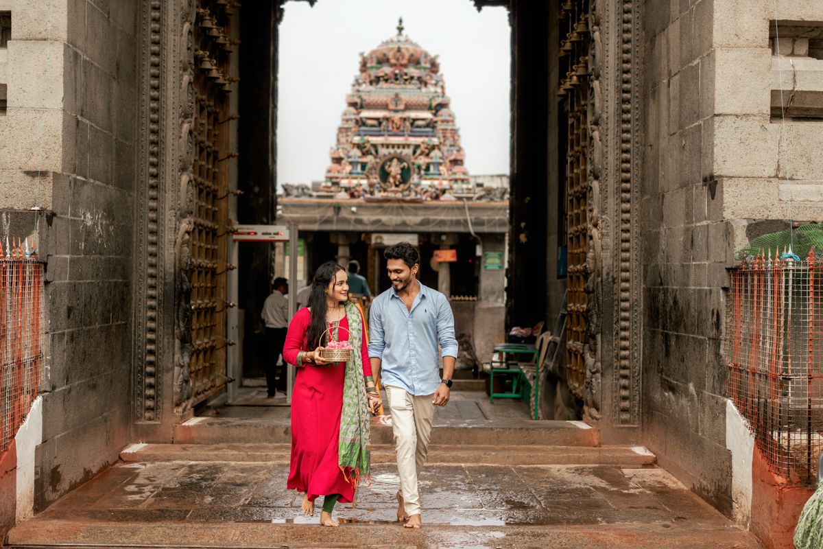 Architectural corridor view of a traditional South Indian temple with stone pillars and ornate tower in the background.