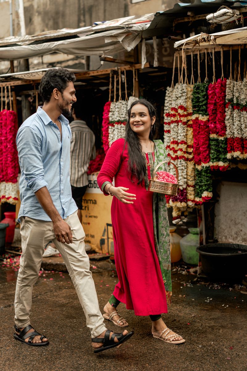A couple walks through a flower market with hanging garlands and decorations in traditional Indian style.