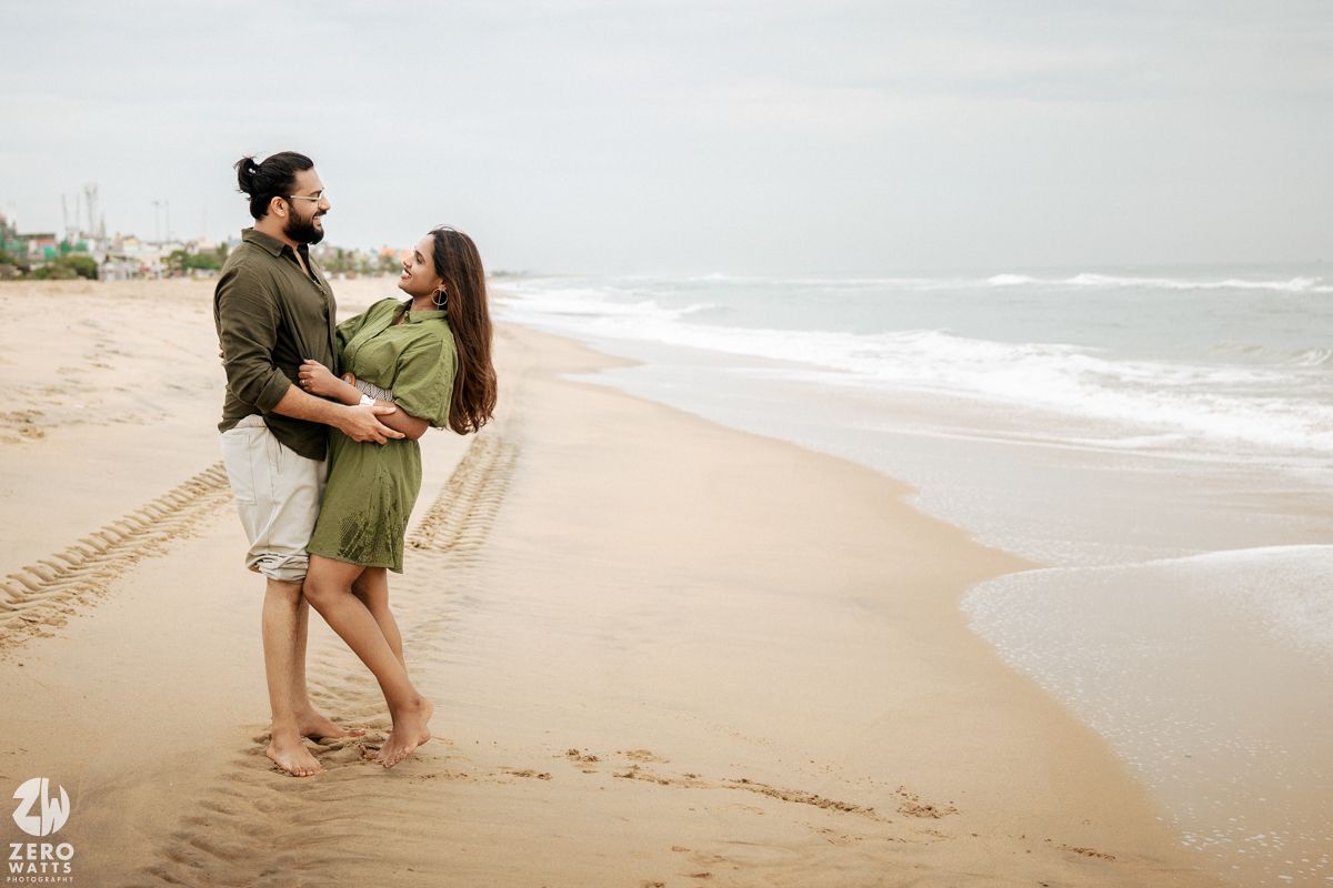 Two people playfully dancing together on a sandy beach with ocean waves in the background.