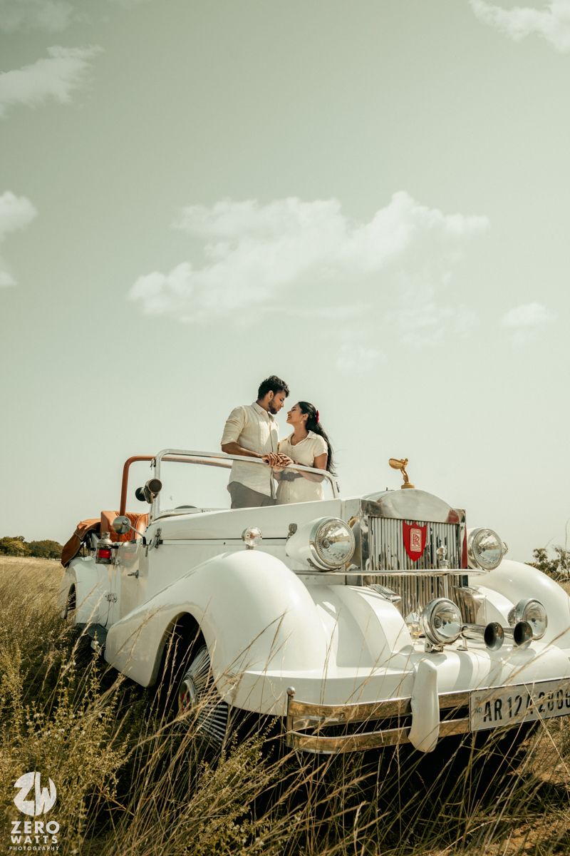 A white vintage luxury car stands majestically in a grassy field under a soft cloudy sky.