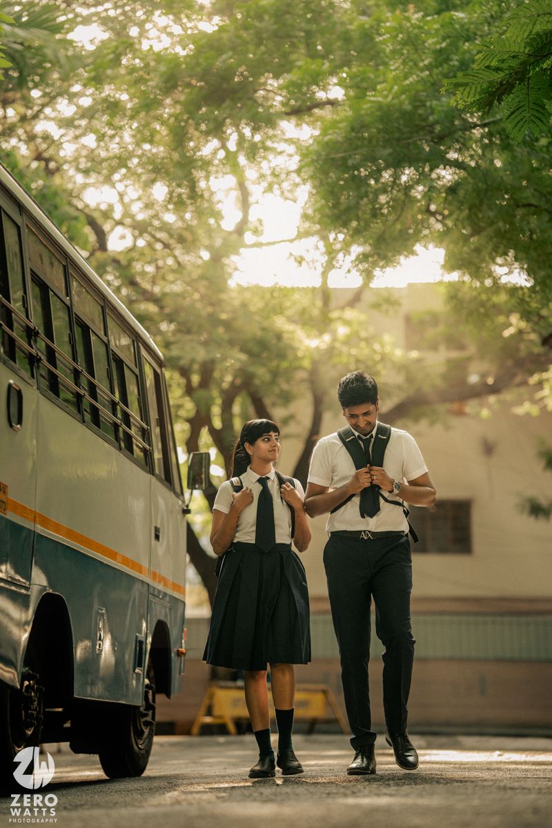 Students in uniforms stand beside a parked bus in dappled sunlight.