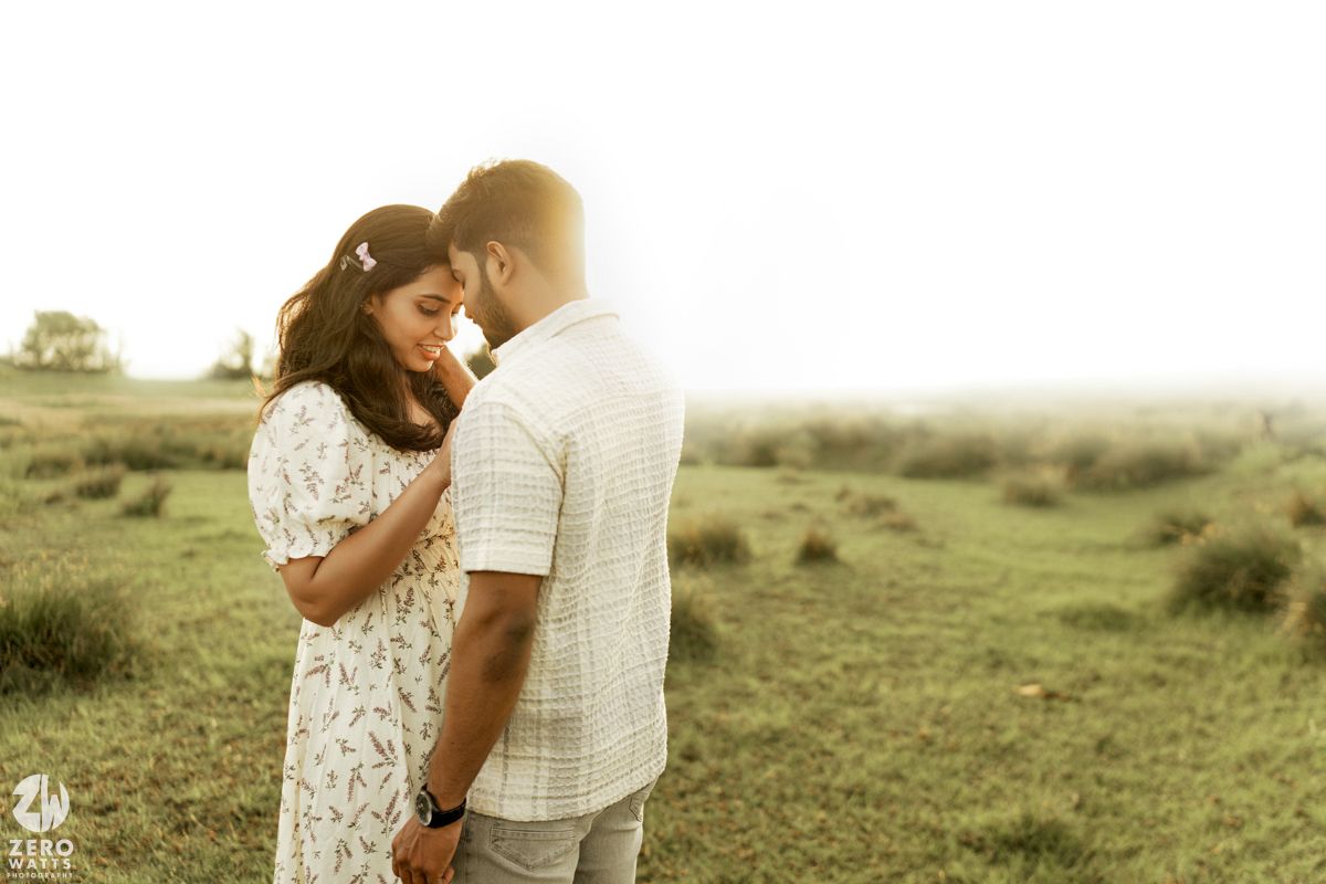 A romantic couple shares an intimate moment in a sun-drenched meadow wearing white and beige clothing.