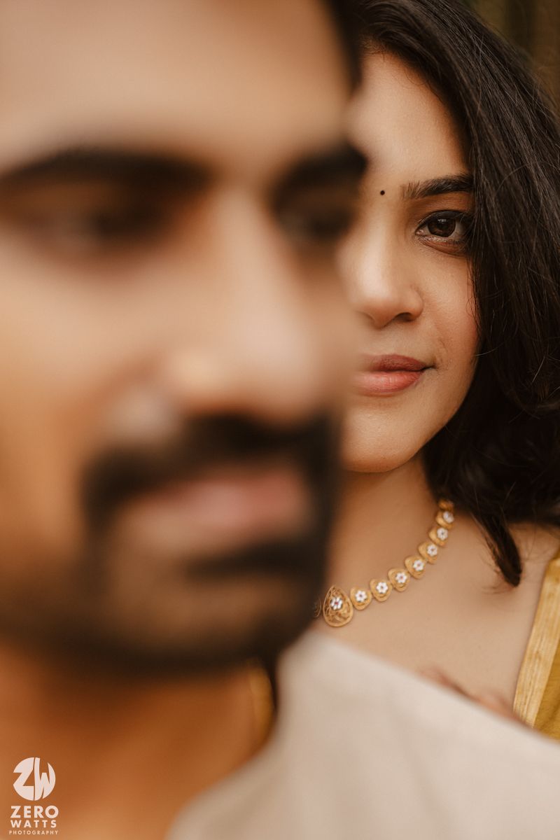 Close-up portrait shot against a warm brown background showcasing delicate pearl earrings and soft lighting.