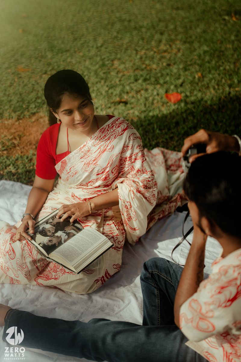 Person in red and white floral dress reads book while relaxing outdoors on grassy lawn.