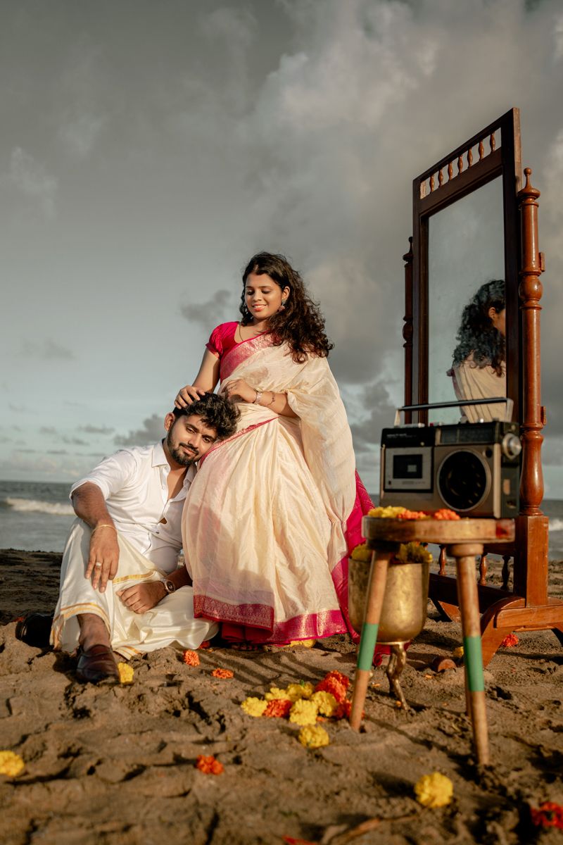 Artistic beach portrait with antique mirror and floral arrangements on moody coastline.