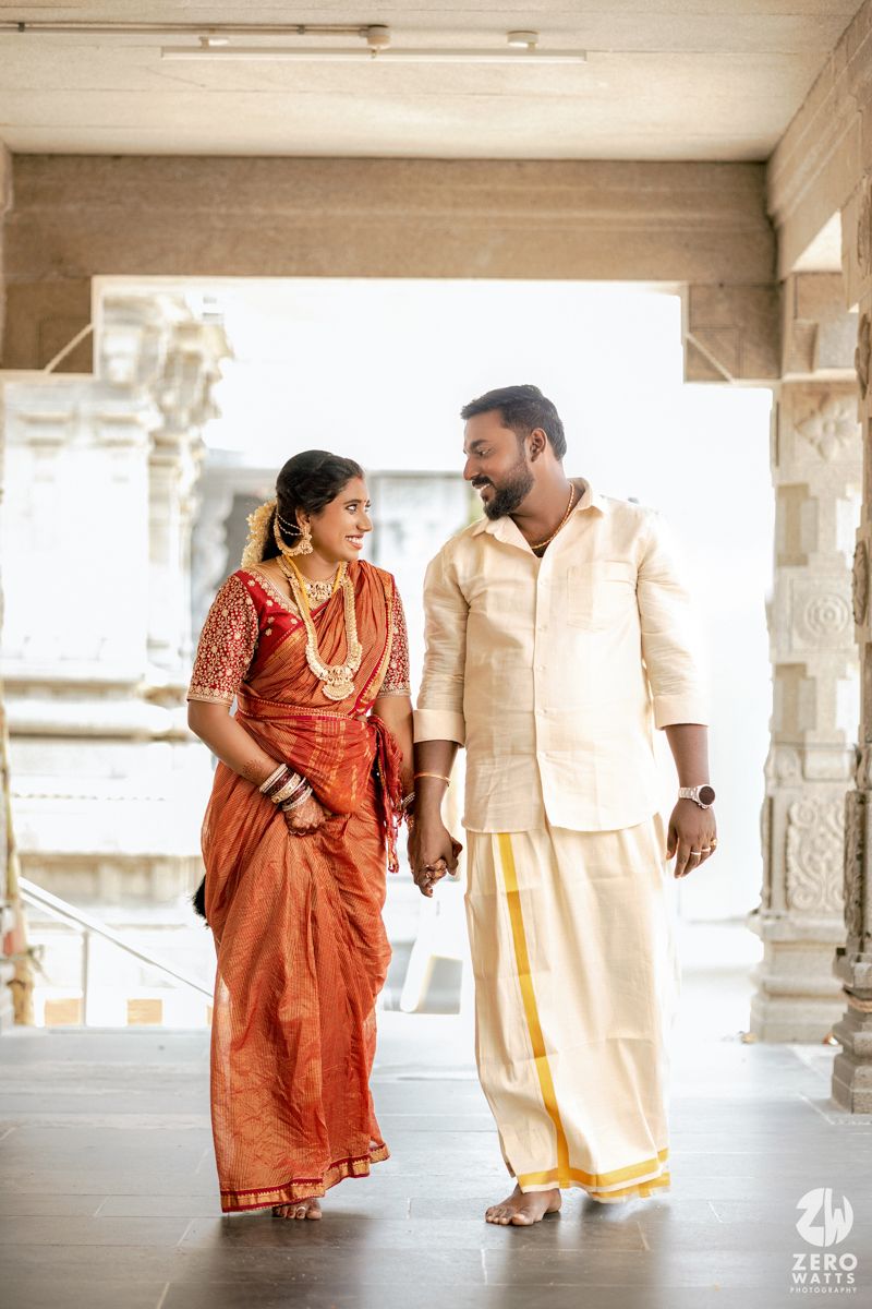 A couple in traditional Indian attire shares candid moments in a pillared corridor.