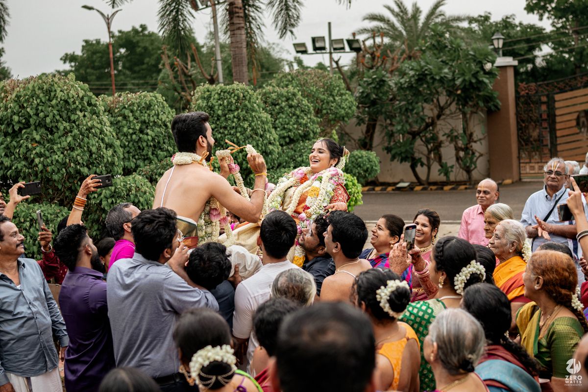 Festive crowd celebrating at outdoor Indian wedding with raised hands and joyful expressions.