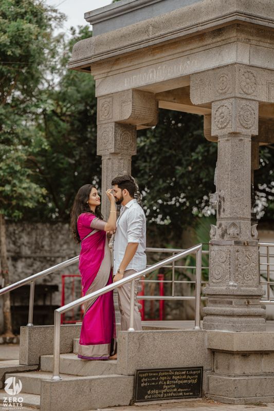 A couple shares an intimate moment beneath ornate stone temple pillars and railings.
