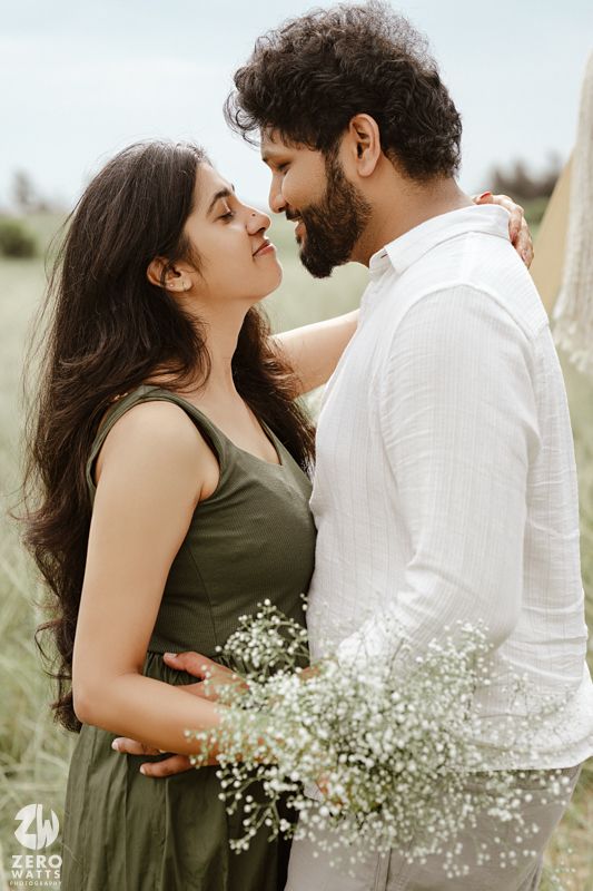 Romantic couple embraces outdoors surrounded by delicate baby's breath flowers in a natural setting.