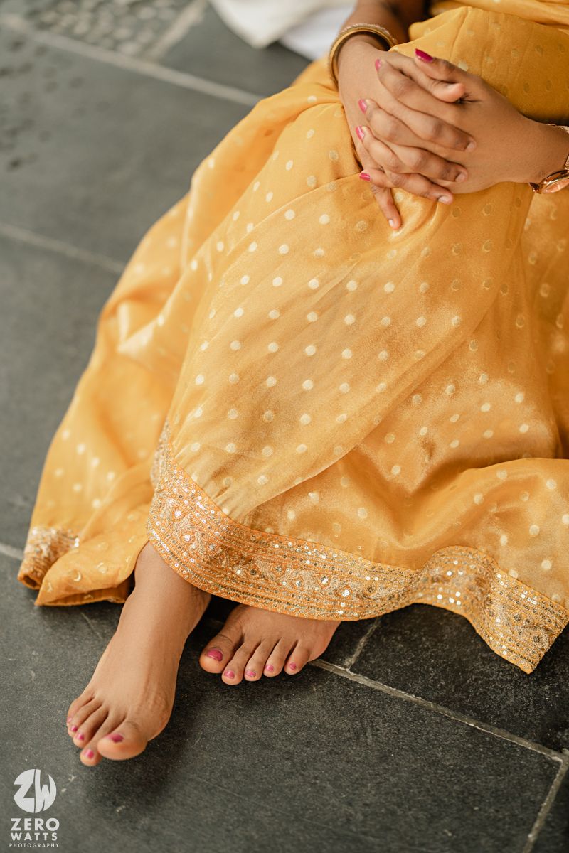Close-up view of bare feet on stone floor with edge of a golden yellow dress visible.