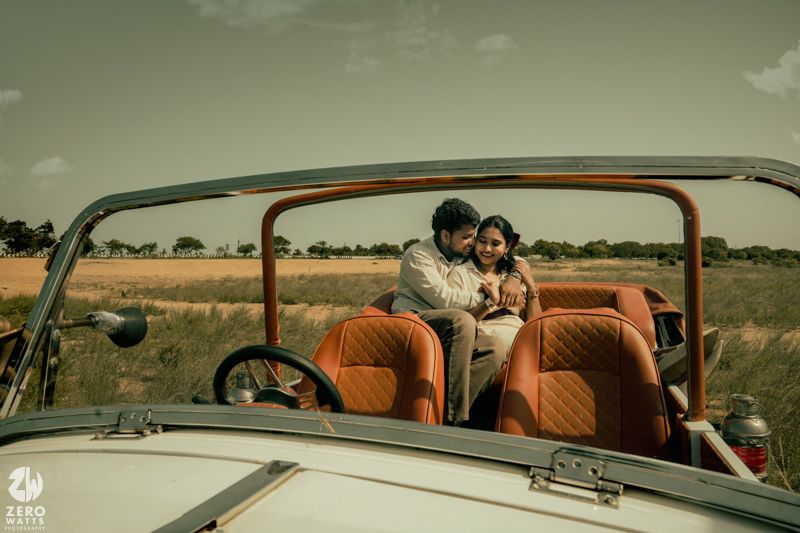 A classic white convertible car with tan interior is shown from a side angle in a rural setting.