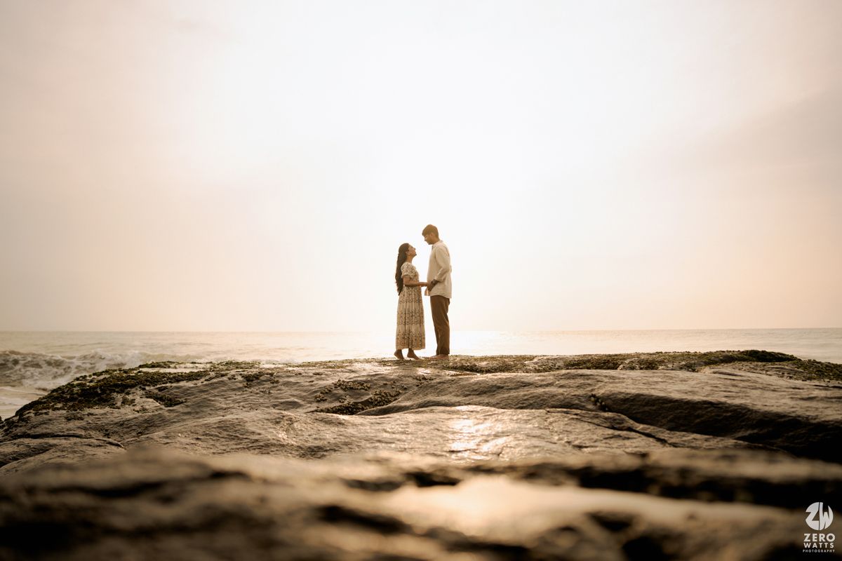 Romantic sepia-toned scene of couple on rocky beach overlook during golden hour.