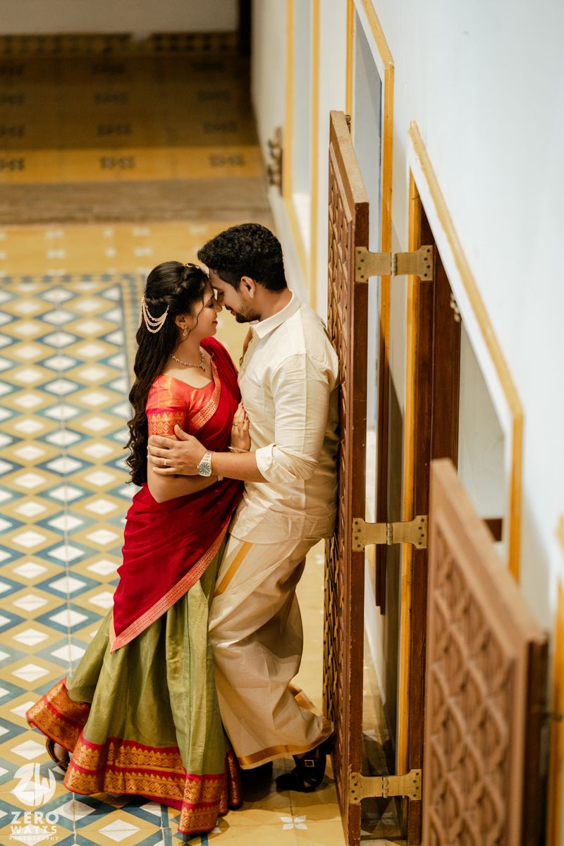 Couple in traditional South Indian wedding attire sharing an intimate embrace in a tiled corridor.