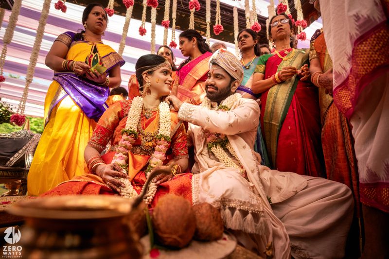South Indian Hindu wedding ceremony with bride in red saree and groom in white sherwani exchanging garlands at mandap.