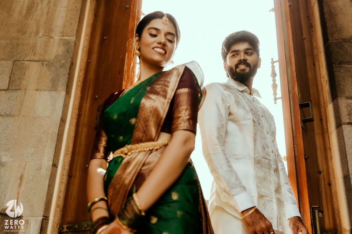 South Indian couple in traditional wedding attire pose elegantly at ornate temple entrance low angle shot.