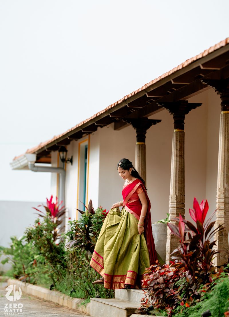 Bride in red and green silk saree standing on veranda of traditional South Indian heritage home.