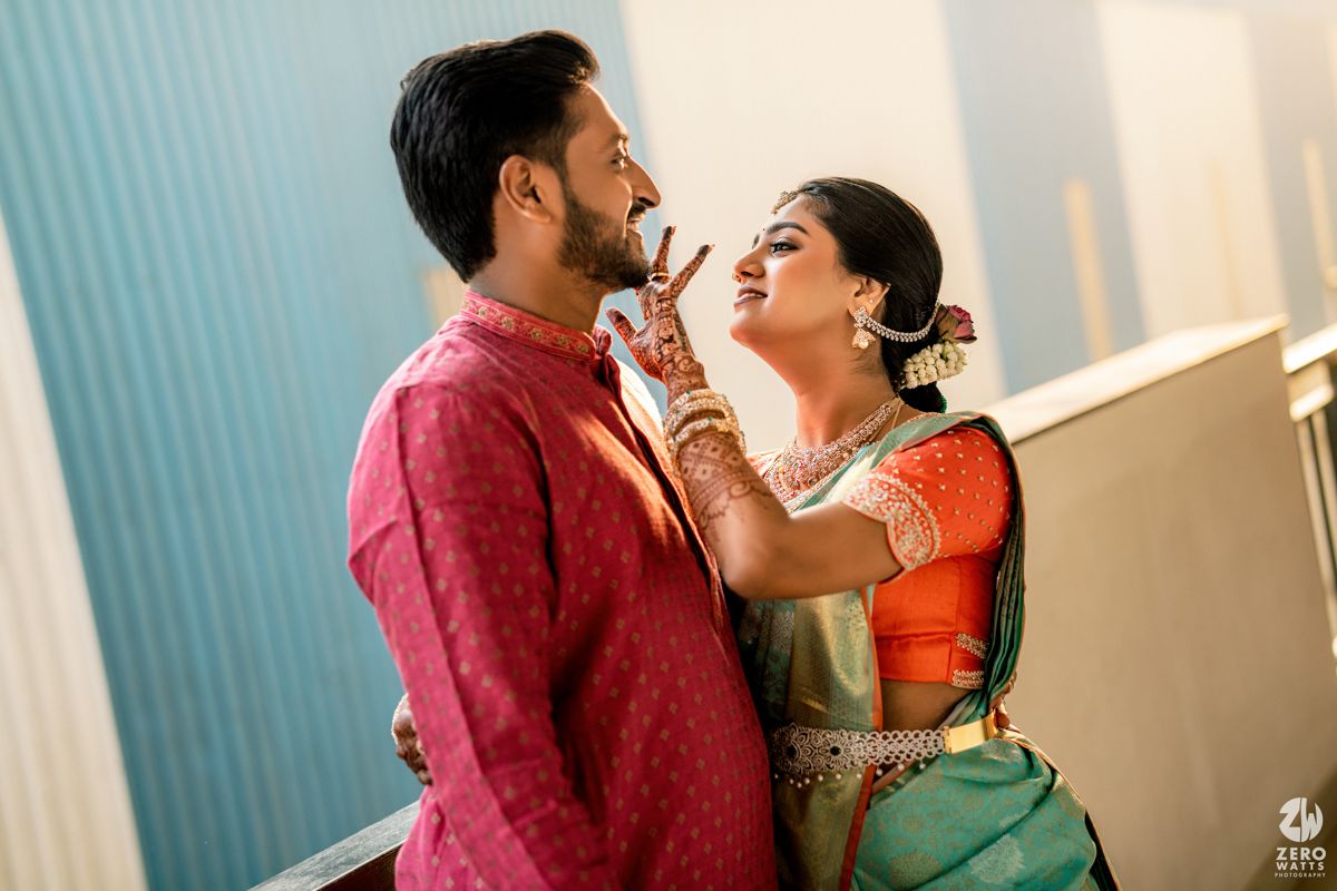 Indian couple in traditional wedding attire, bride in green saree feeds groom in red kurta during ceremony.