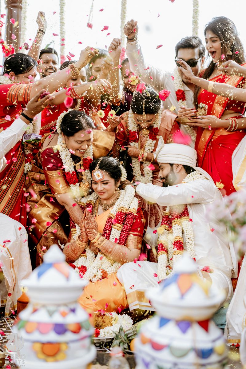 Joyful South Indian wedding ceremony with couple surrounded by guests throwing flower petals.