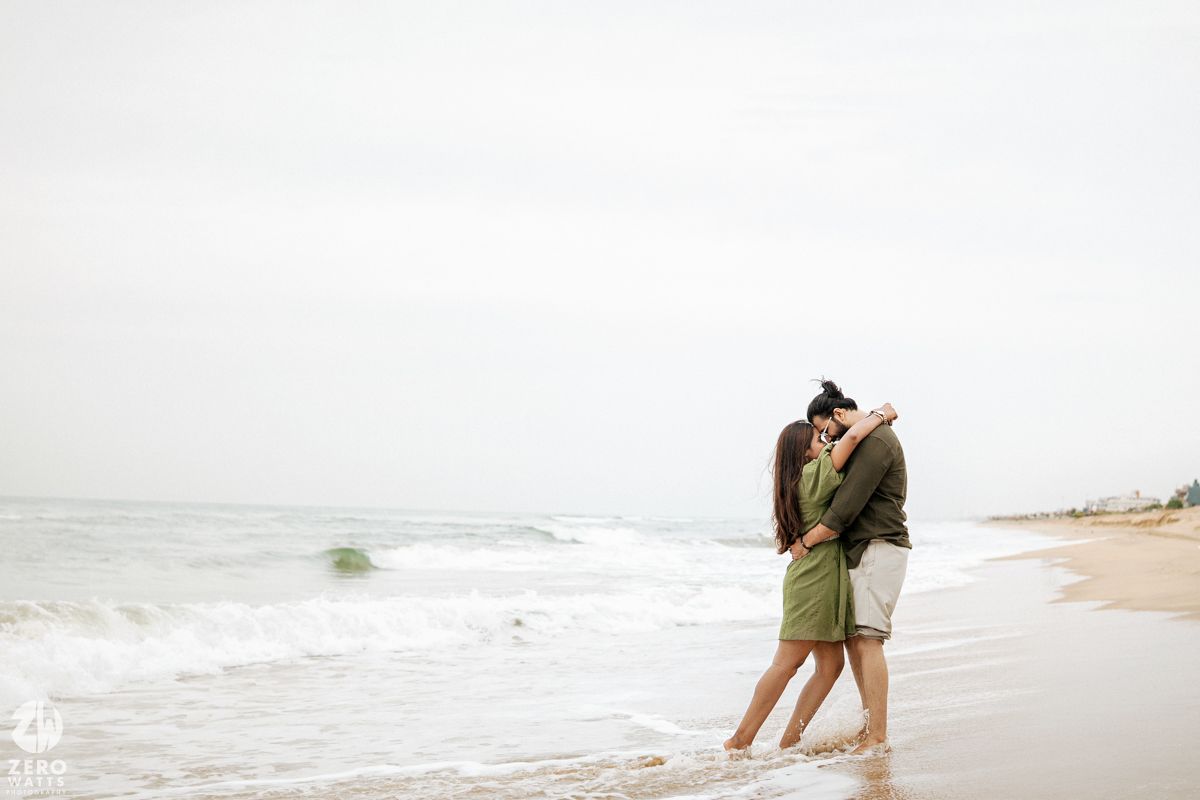 Two people stroll together on a peaceful sandy beach with waves in the background.