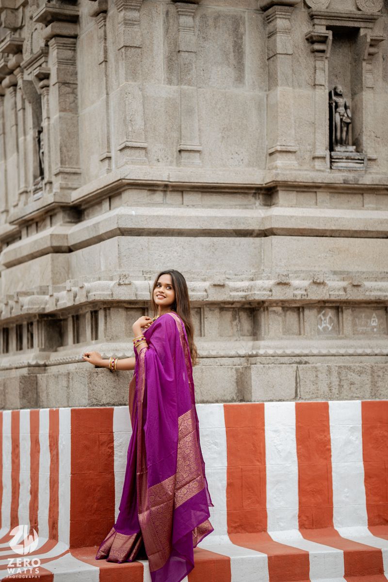 Woman in purple sari poses along red and white striped temple wall in artistic photoshoot.
