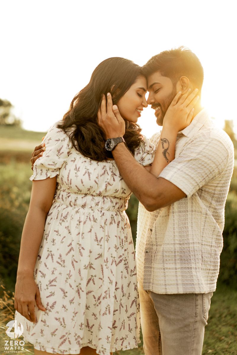 A tender moment between a couple in summer attire against warm sunlit backdrop.