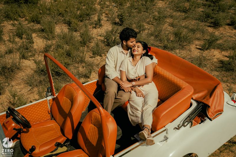 A vintage orange and white convertible car parked in a desert landscape.