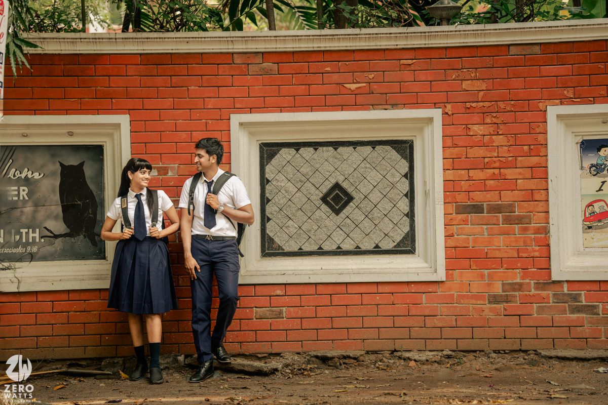 Students in uniforms standing near a red brick wall with decorative windows.