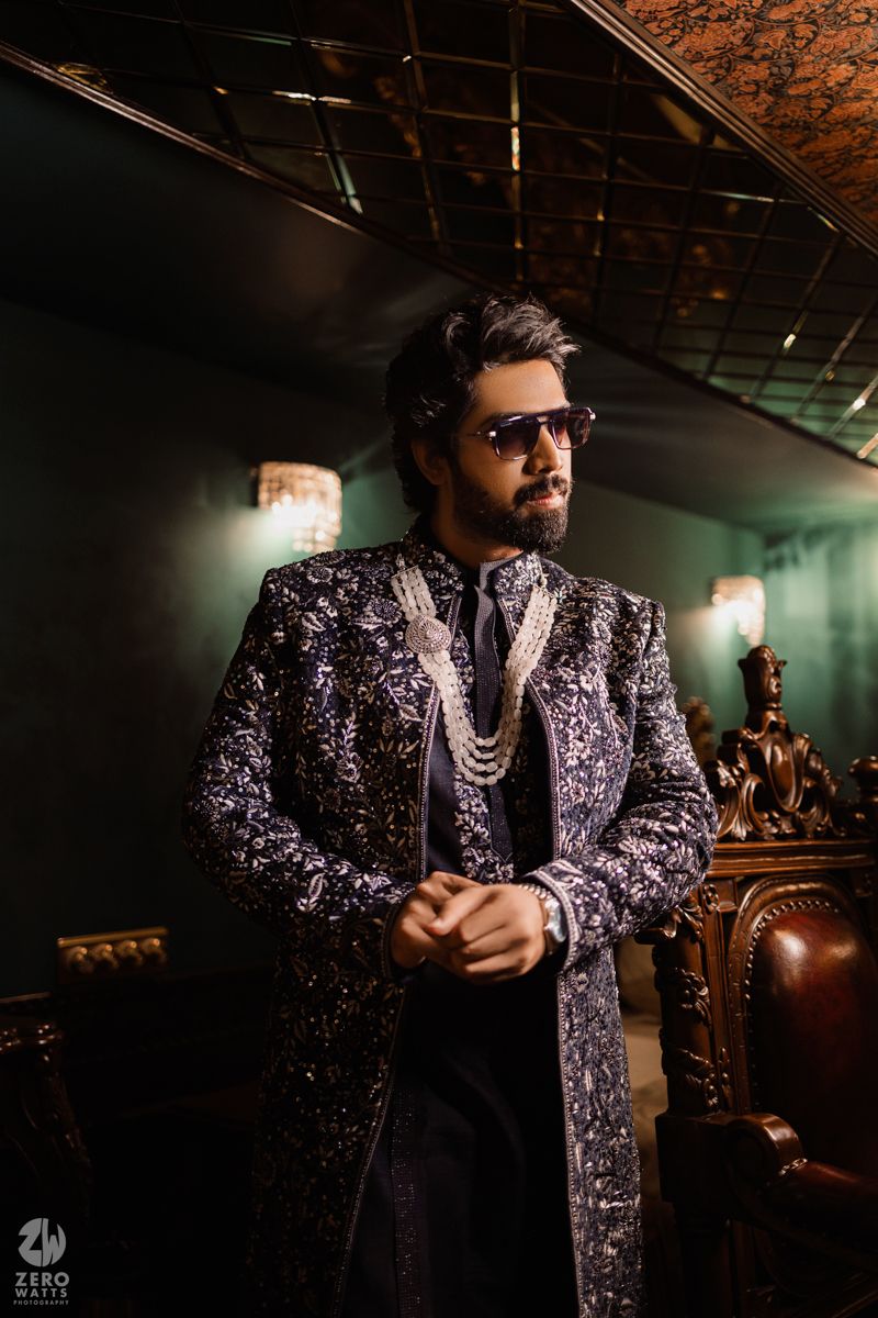 A person in a sparkly purple formal suit poses dramatically in a dimly lit room.