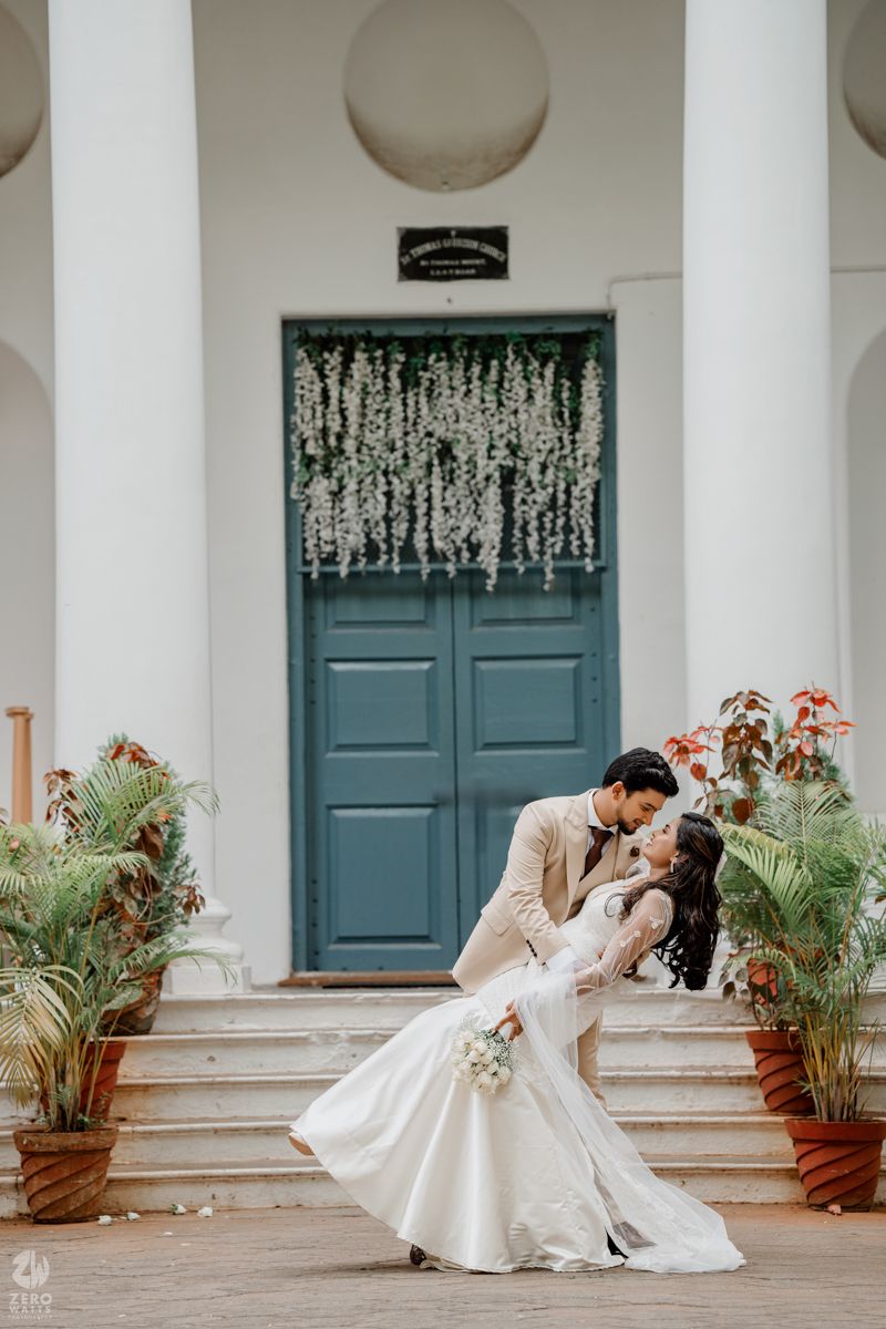 A romantic wedding portrait of a couple posing in front of a teal door with hanging white flowers.