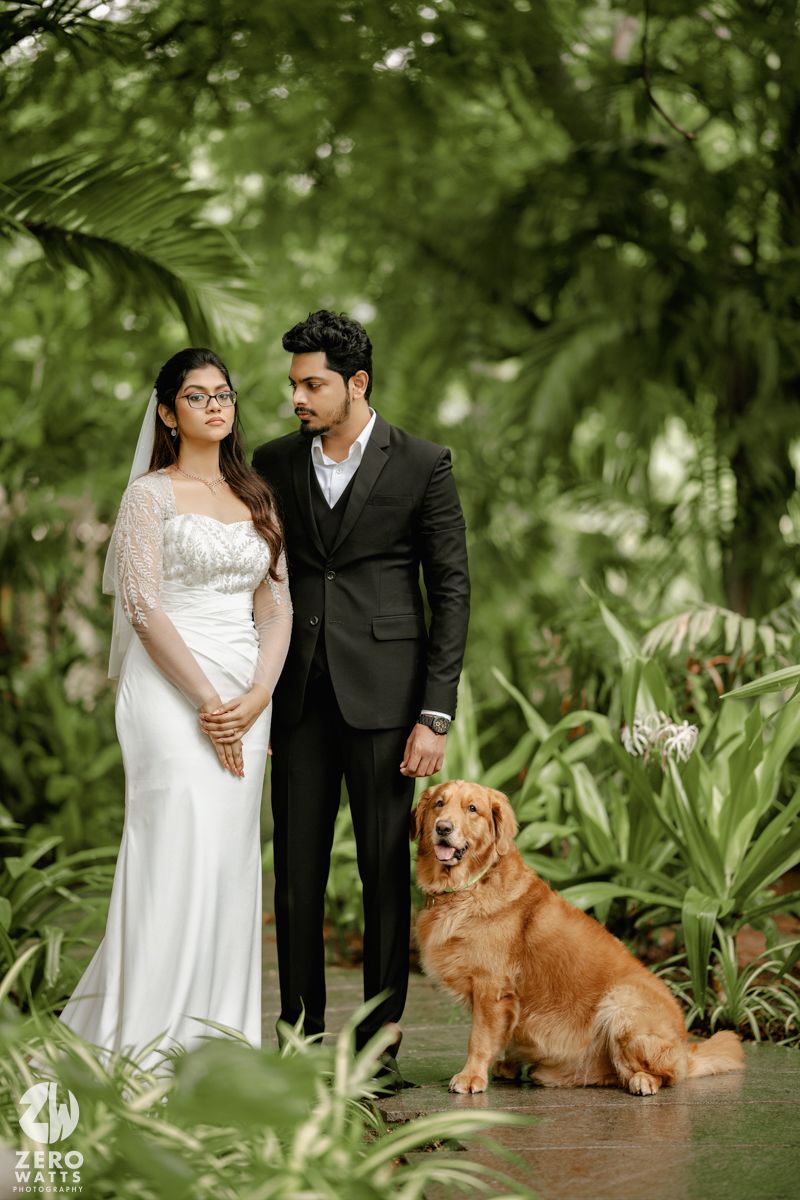 A romantic wedding photoshoot in a lush garden setting with a couple in formal attire and their golden retriever companion.