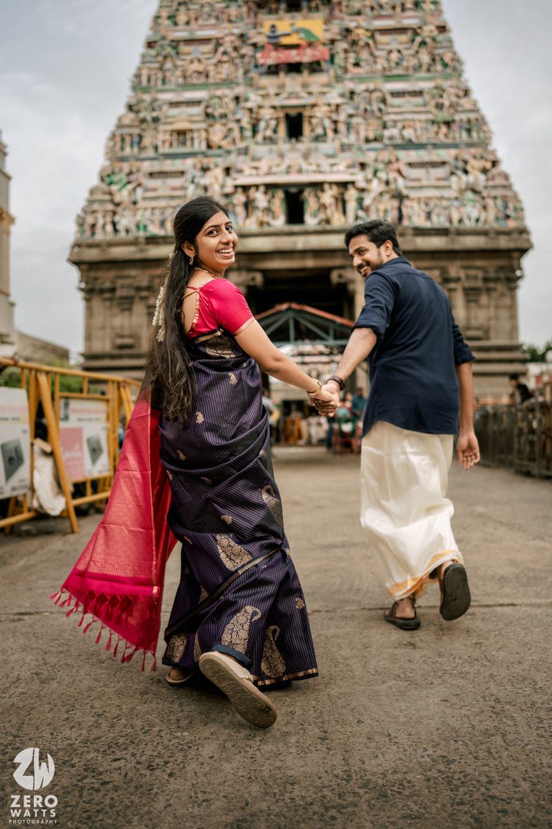 A couple poses playfully in front of an ornate temple gopuram with traditional South Indian architecture.