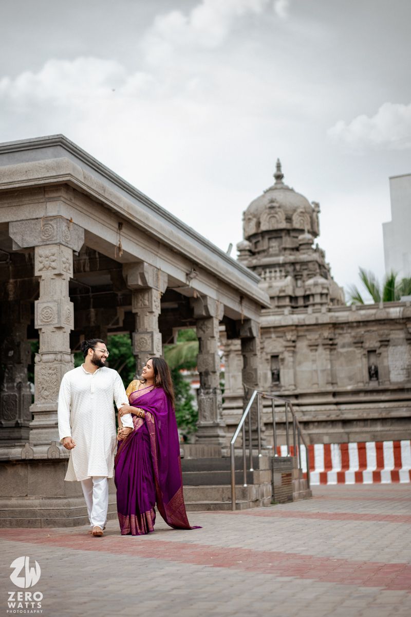 Elegant couple poses in traditional Indian wear at a historic temple with stone pillars and domed architecture.