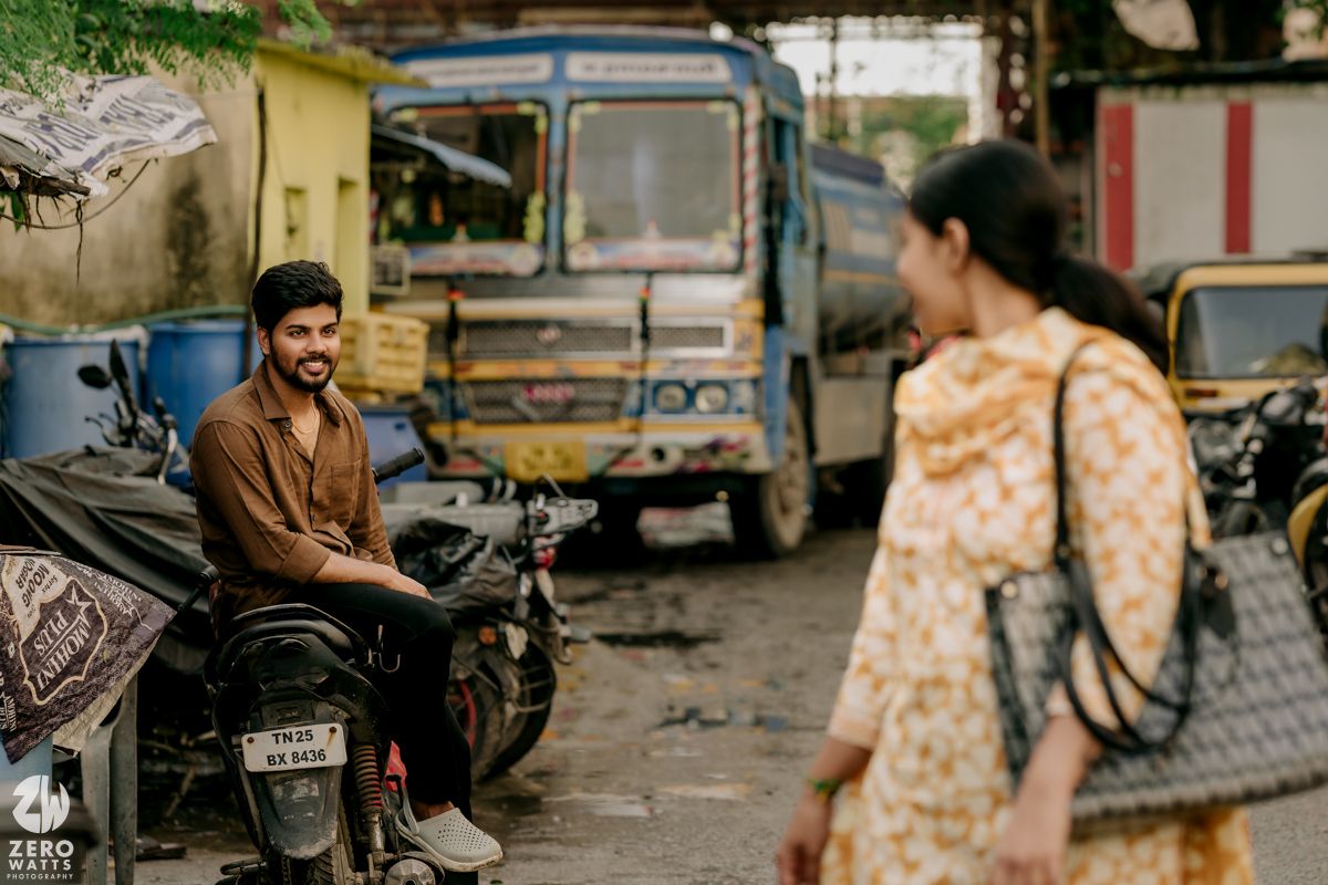 Two people having a conversation near parked vehicles and a bus in an urban neighborhood.