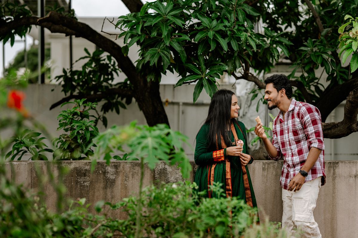 A couple enjoys a romantic moment in a garden with lush green foliage in the background.