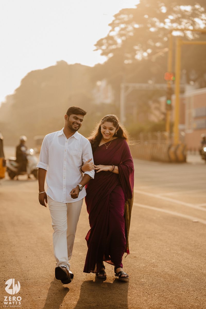 A couple in traditional attire walks together during golden hour on a street.