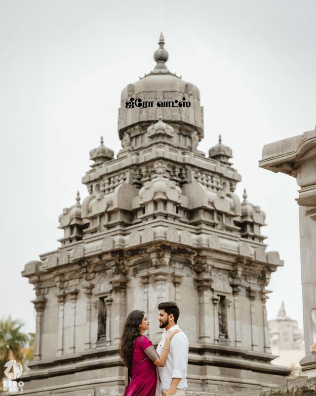 A couple poses near ornate white domed structures with traditional Indian temple architecture.