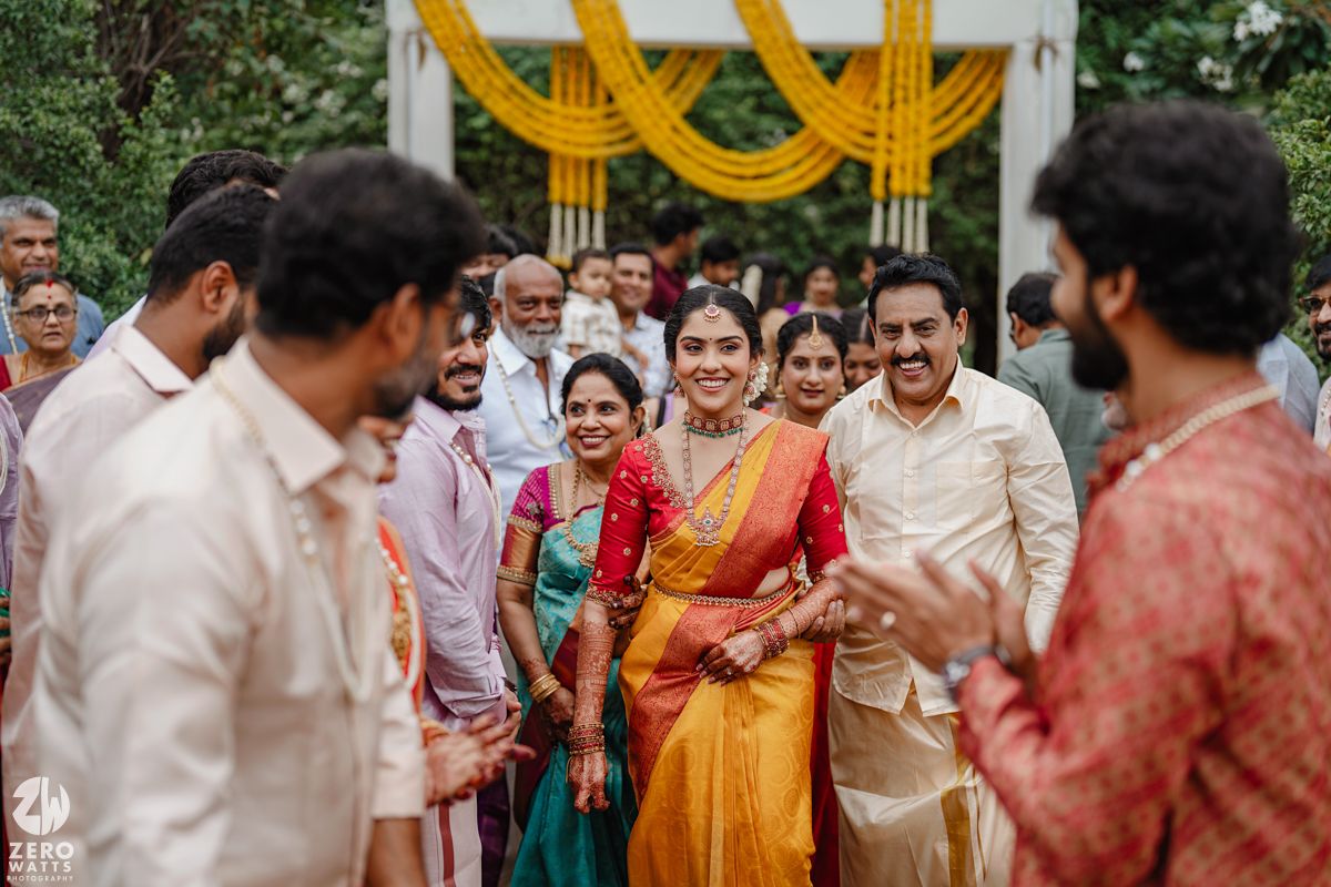 Wedding guests in traditional attire gather around yellow floral decorations at an outdoor celebration.