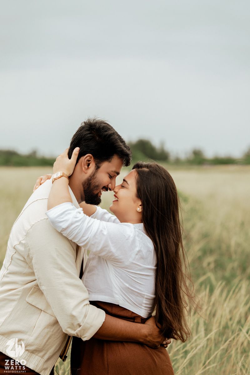 A couple in white and brown outfits share an intimate embrace in tall grass.