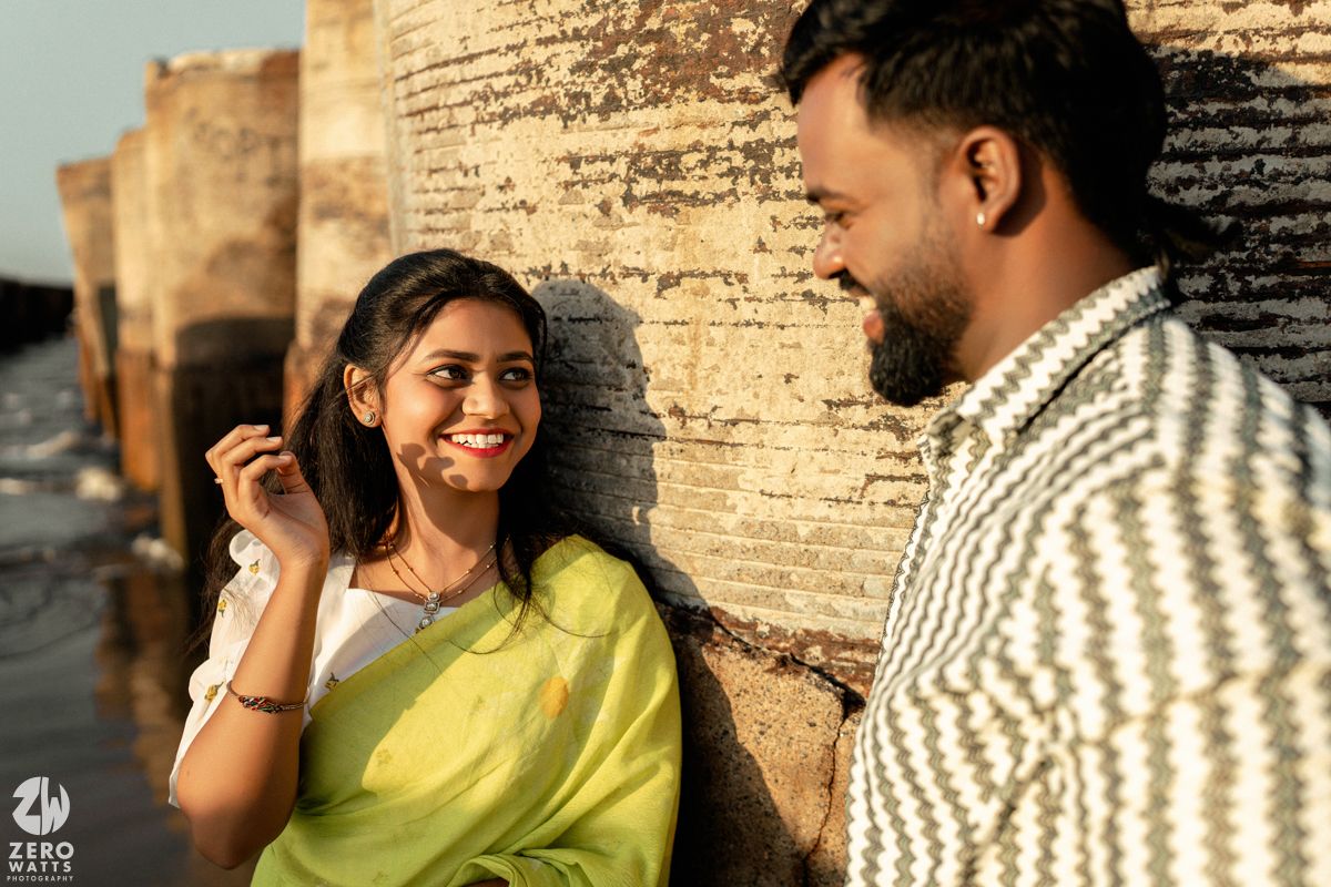 A couple shares a romantic moment against a textured stone wall in warm sunlight.