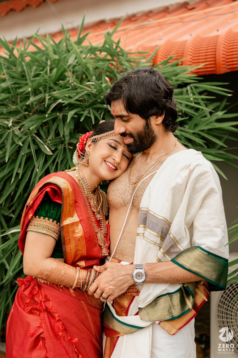 South Indian couple in traditional wedding attire embracing outdoors with lush greenery in the background.