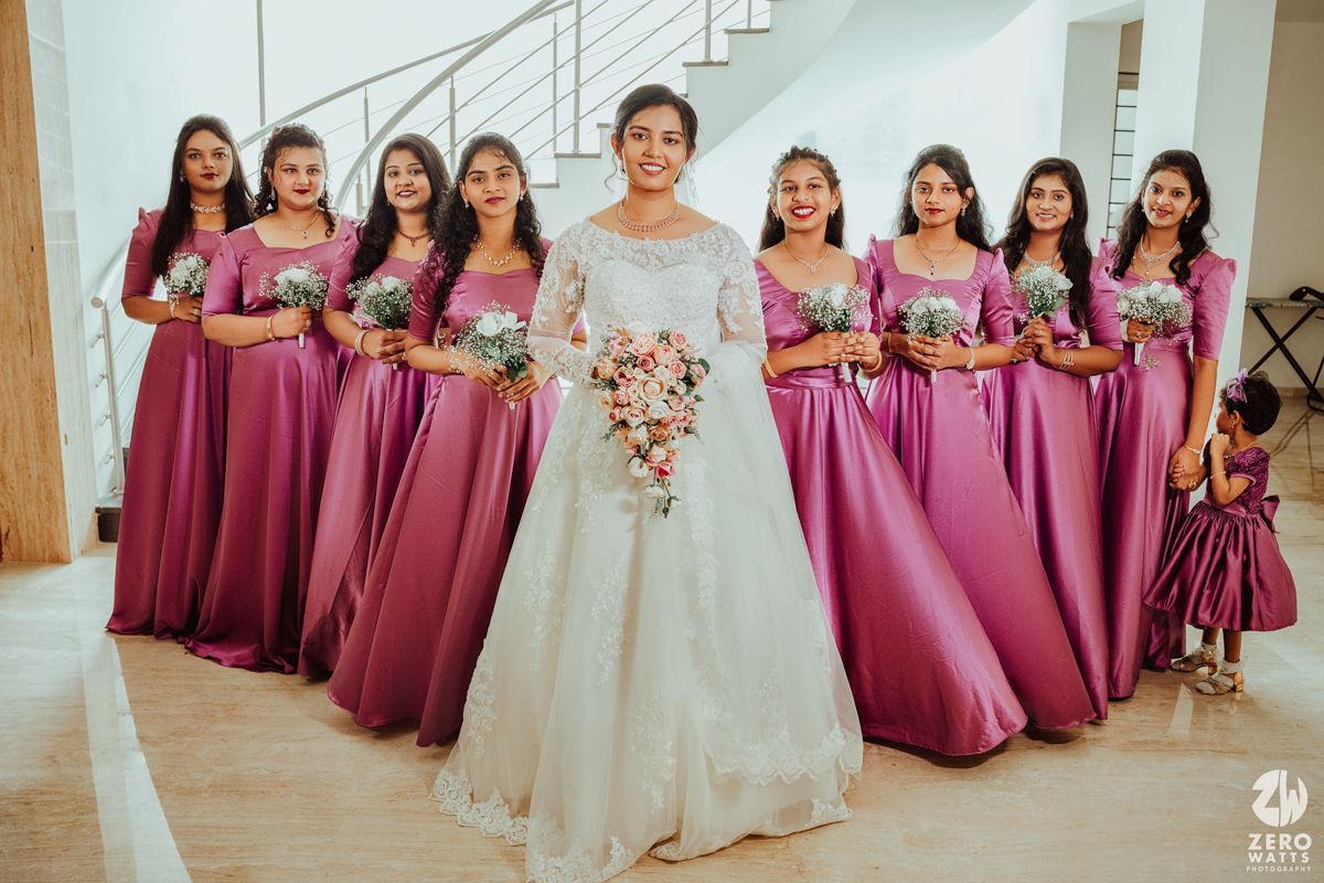 Bridesmaids in magenta dresses pose together in a line with the bride in white at a wedding celebration.