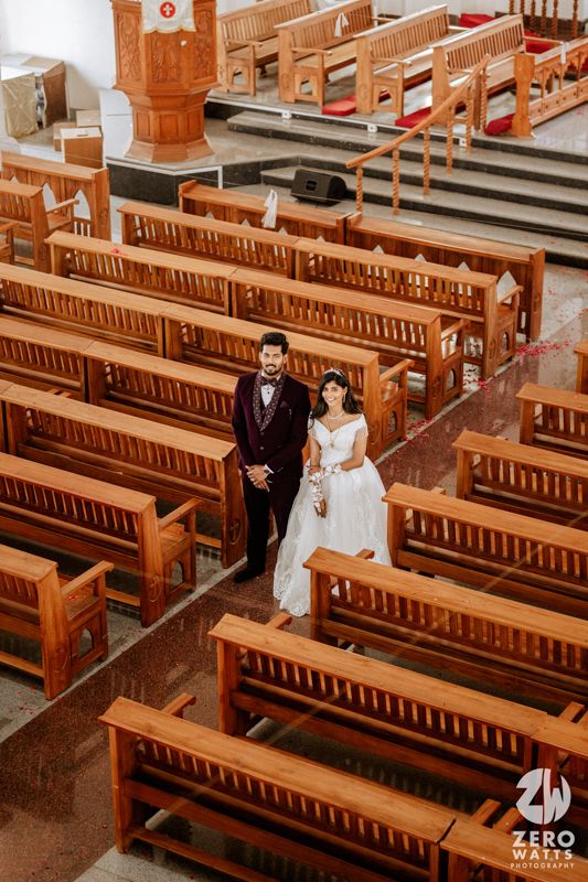 Aerial view of bride and groom walking through empty church aisle surrounded by wooden pews.