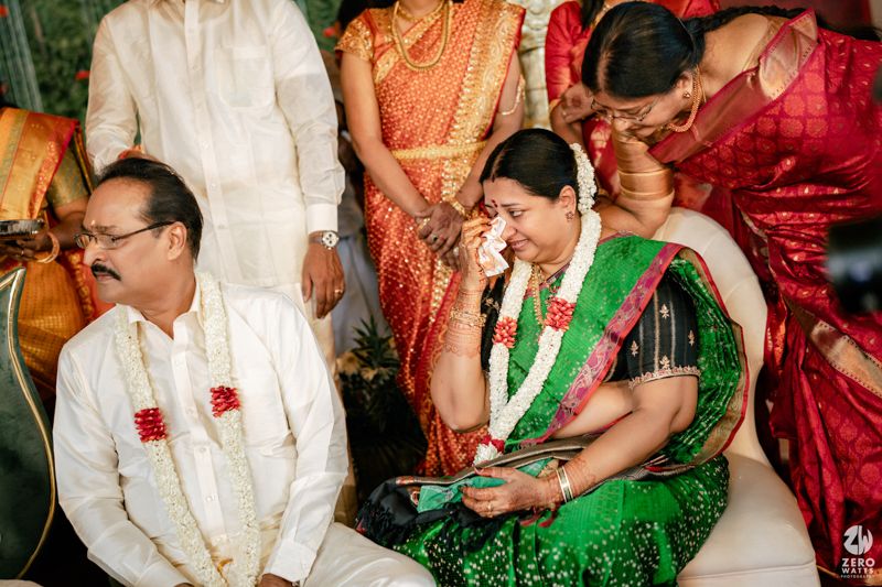 Emotional Indian wedding ceremony moment with bride in green Kanjeevaram saree wiping tears surrounded by family members.