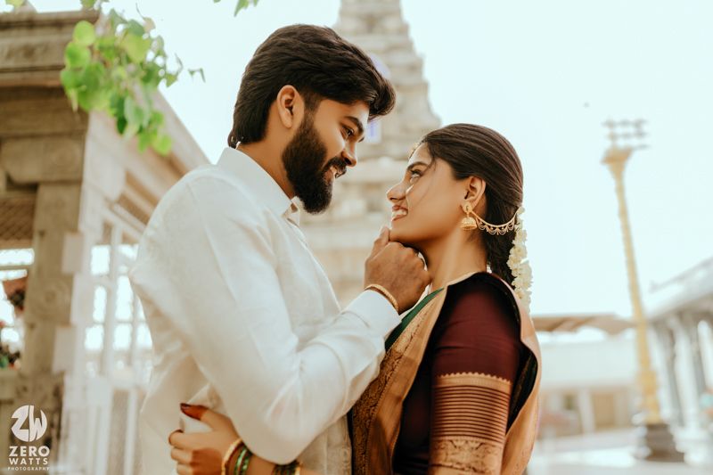 Indian couple in traditional attire share a romantic moment near a temple during a pre-wedding photoshoot.
